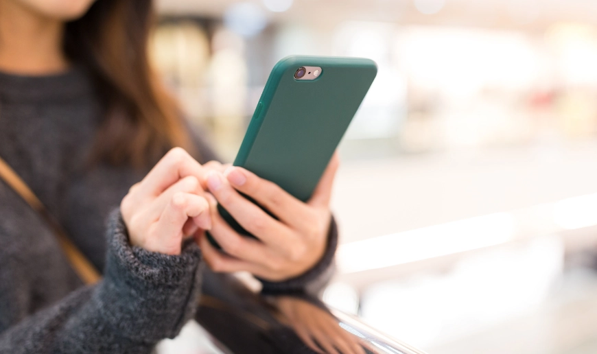 Person använder mobiltelefon och skriver med ena handen i offentlig miljö suddig bakgrund med fokus på telefonen