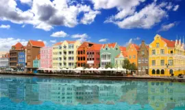Färgglada hus längs hamnen i Willemstad på Curaçao under en blå himmel med moln. 