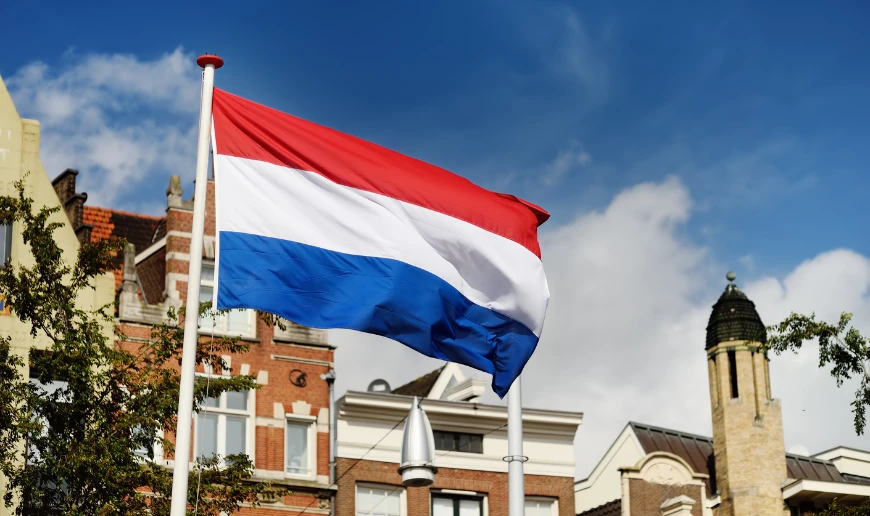 Nederländernas flagga vajar framför byggnader under en blå himmel